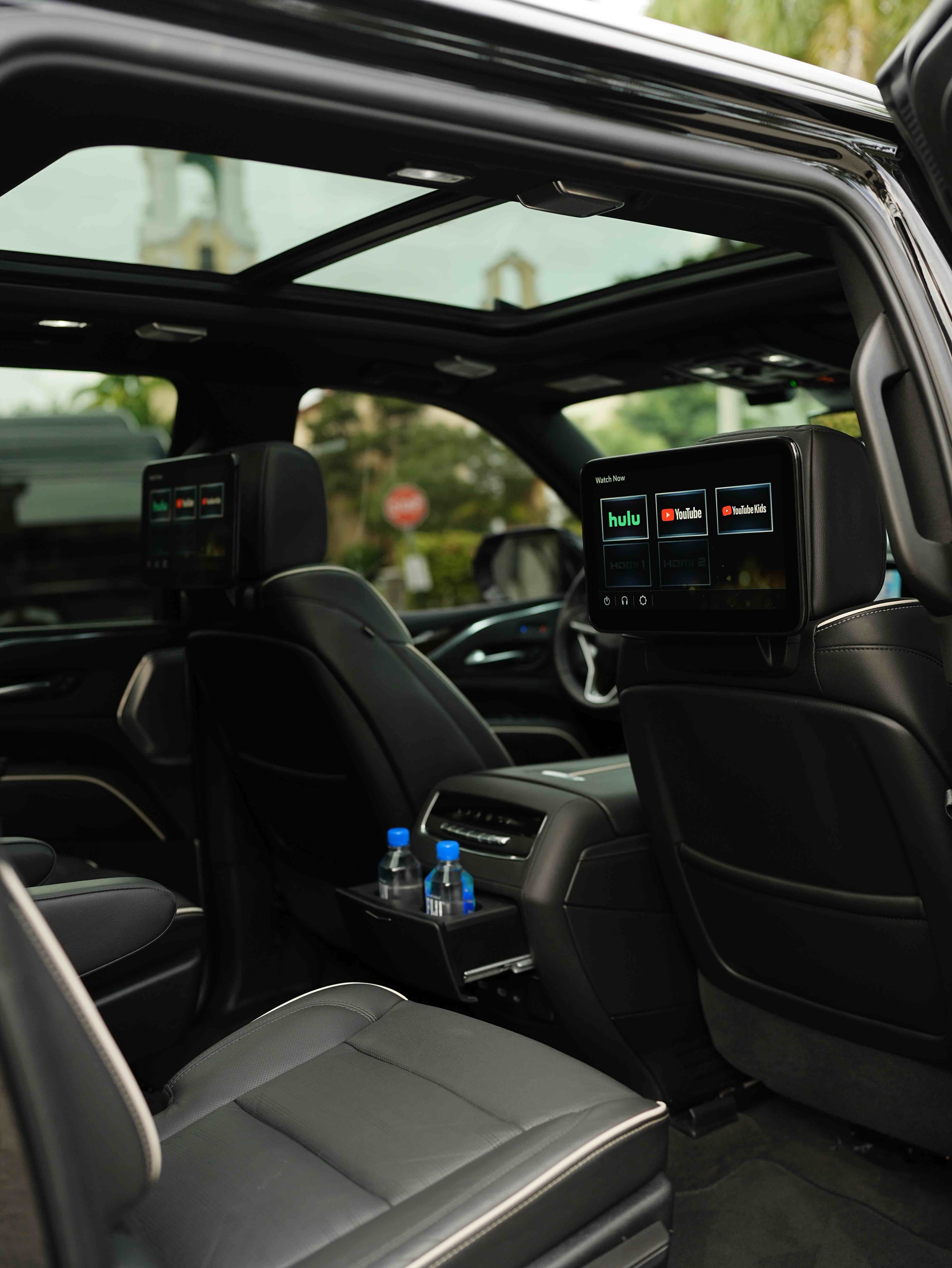 Rear cabin of a chauffeured Escalade with seat-back screens and refreshments
